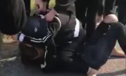 2 thiếu nữ nằm rạp xuống đất đau đớn chịu đòn, nhiều nam thanh niên đứng quay clip